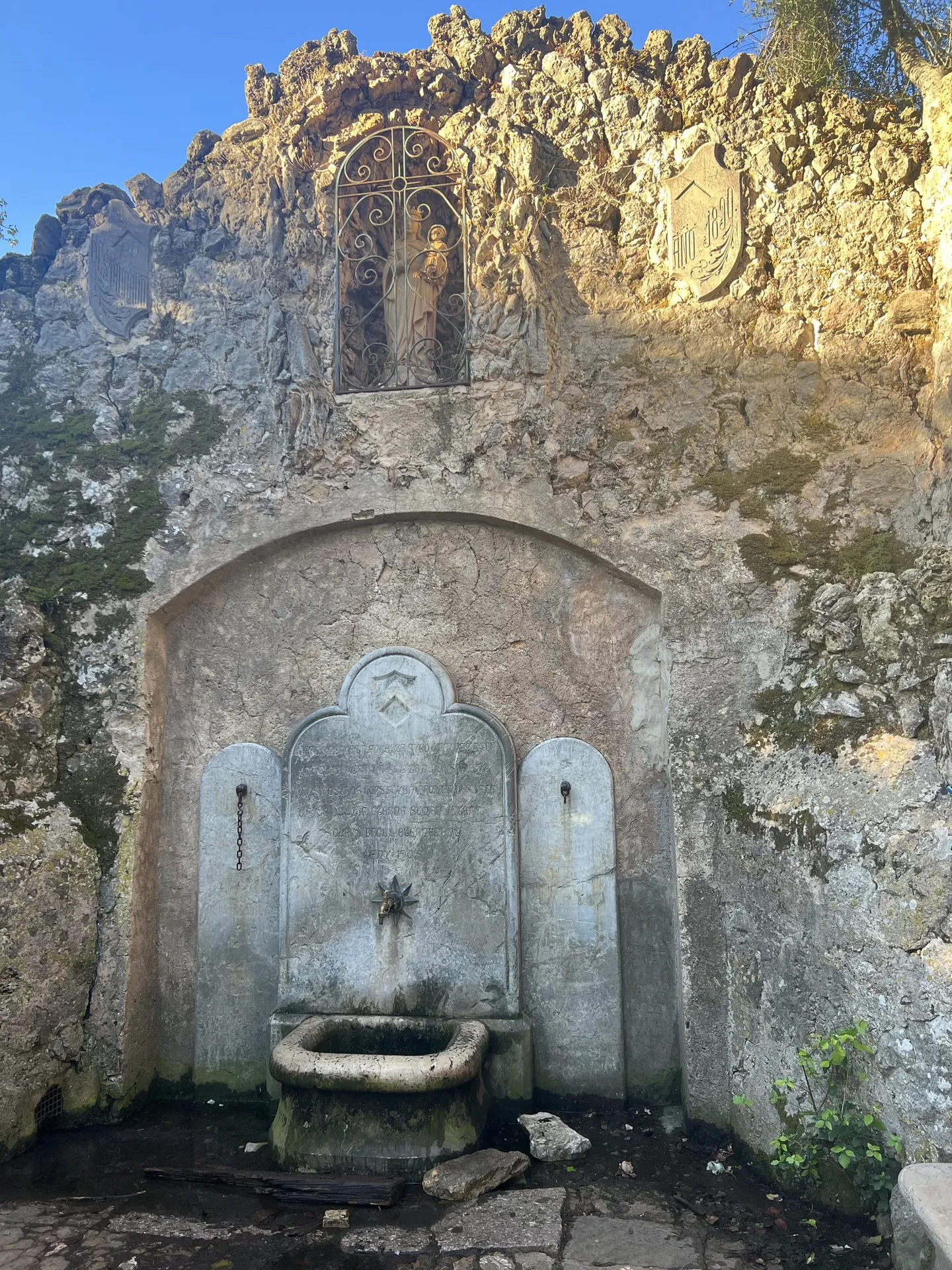 Alter Steinbrunnen mit Quellwasser an einer Felswand.