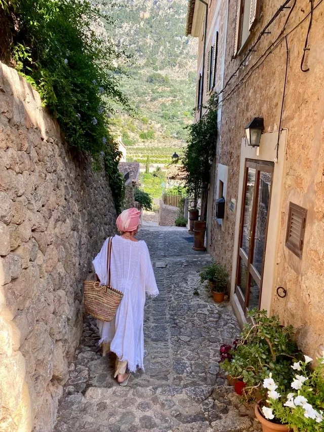 Frau in weißem Kleid geht eine gepflasterte Gasse in Biniaraix hinunter