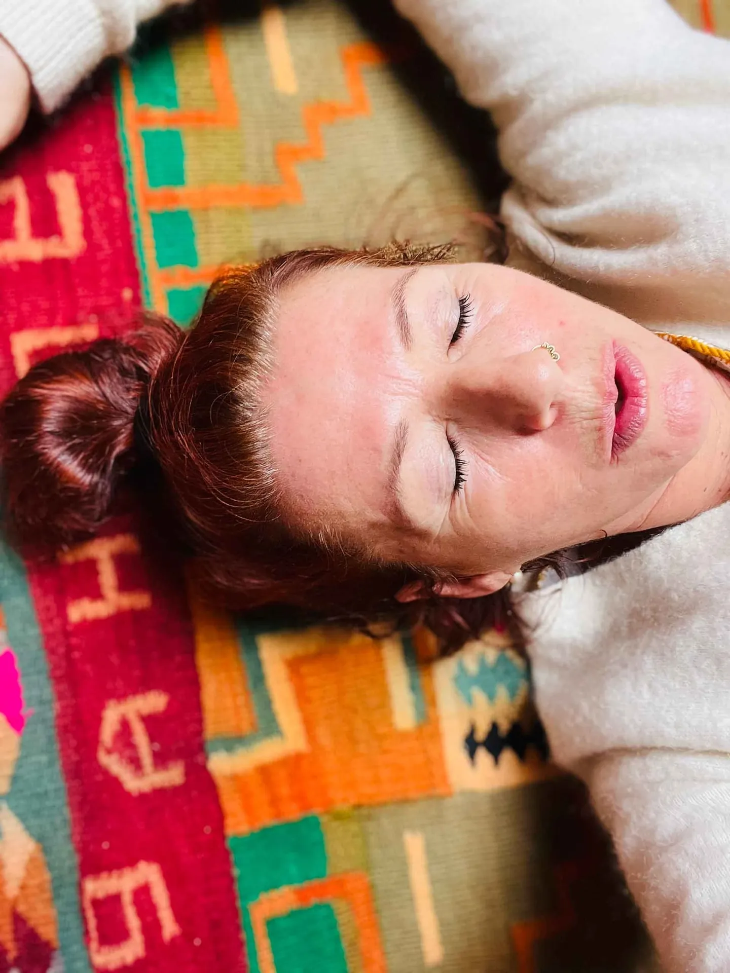 Frau liegt mit geschlossenen Augen entspannt auf einer bunt gewebten Decke.