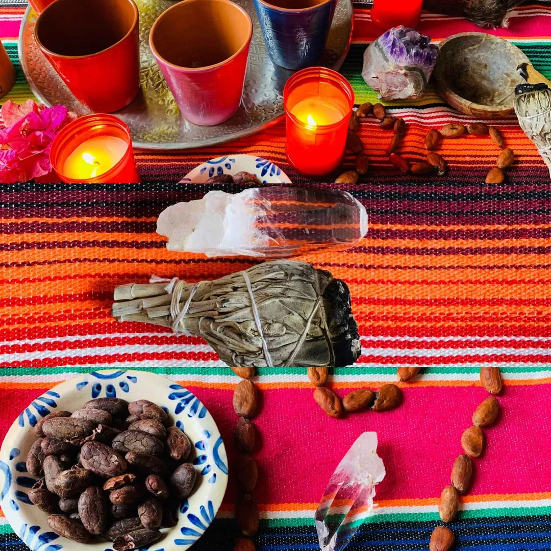 Cacao-Altar mit zwei Bechern, Kristallen, Räuchersalbei und Kakaobohnen auf einem bunt gewebten Tuch.