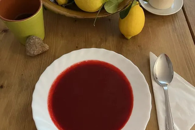 Tiefrote Fastensuppe auf einem weißen Teller auf einem Holztisch, daneben frische Zitronen, eine Tasse Tee und ein Herzstein.