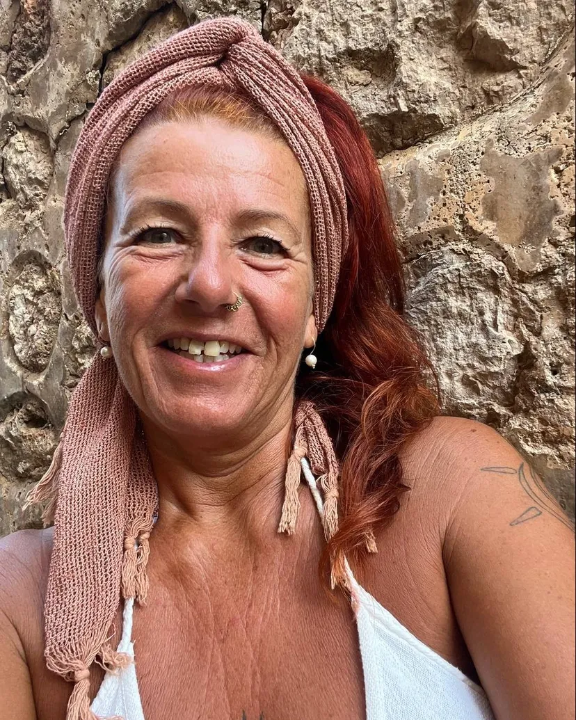 Marion Khalsa Kaur mit rosa Kopftuch, lächelnd vor einer Steinwand