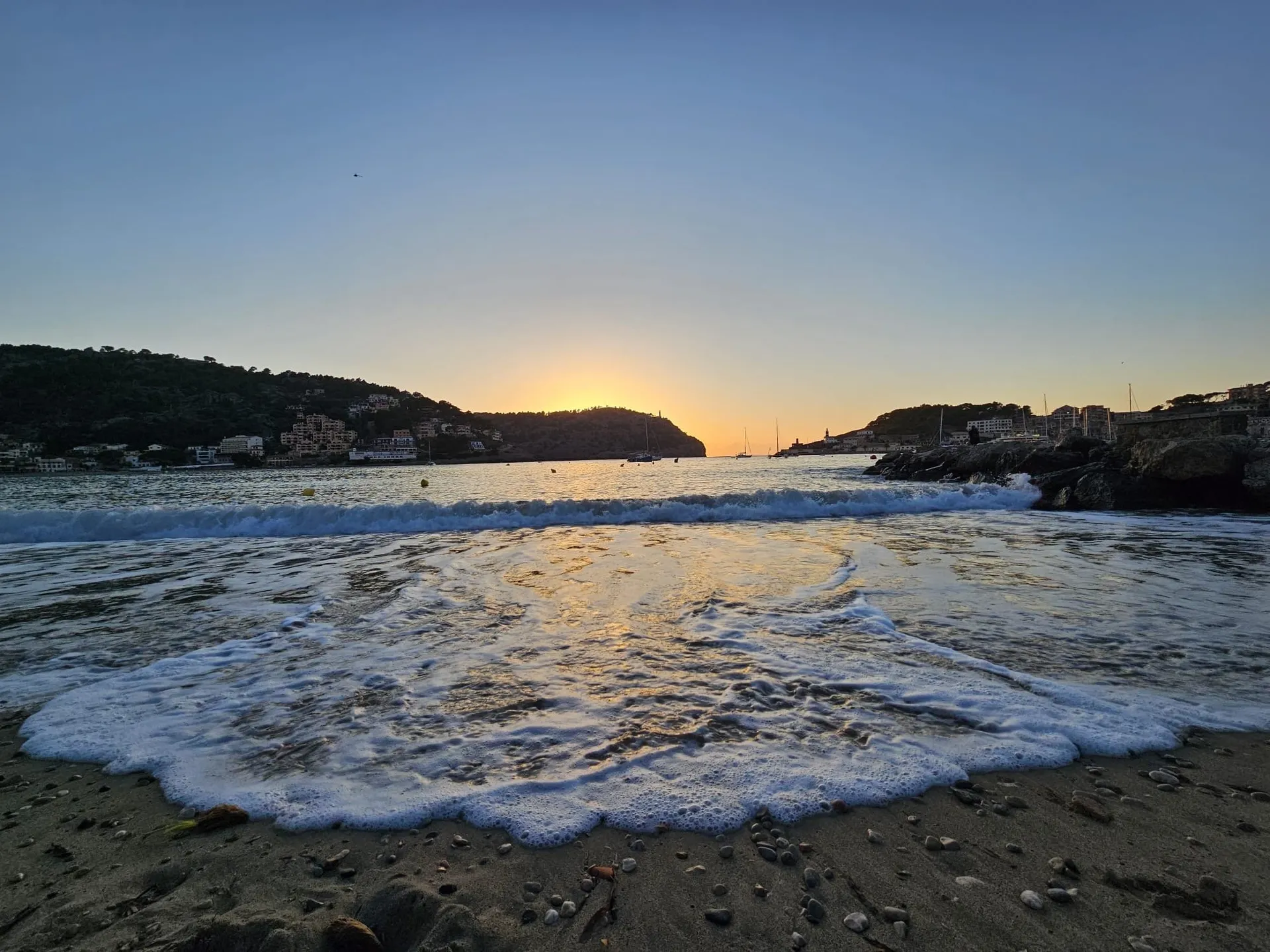 Sonnenuntergang über einer Bucht mit sanften Wellen an einem Strand auf Mallorca