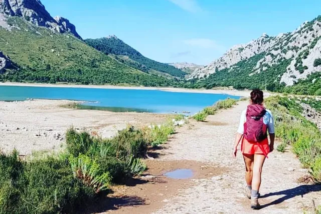 Frau mit Wanderrucksack auf einem Weg an einem türkisfarbenen Bergsee im Tramuntana-Gebirge